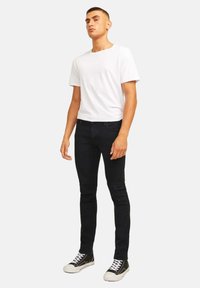 T-shirt bianco a maniche corte abbinato a jeans slim-fit neri e sneakers nere con lacci bianchi e suole in gomma. Design semplice.