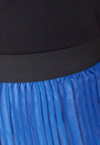 Cintura elástica negra por encima de una falda azul plisada con rayas verticales, hecha de una tela ligera y transparente.