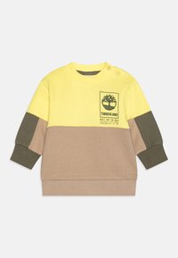 Felpa gialla e beige con dettagli verde oliva, dotata di una toppa con logo e bottoni a pressione sulla spalla. Materiale morbido in misto cotone.