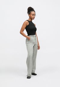 Čierny bezrukávový top s vysokým výstrihom v kombinácii so svetlošedými džínsami širokého strihu s prednými vreckami a čistými švami. Čierne topánky dopĺňajú outfit.