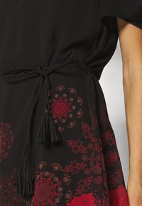 Černé šaty s červenými květinovými vzory, propletenou černou stuhou v pase a střapci na koncích stuhy. Hladká textura látky.