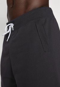 Bermudas de algodão pretas com cós elástico e bolso lateral; textura suave e um corte relaxado para conforto.