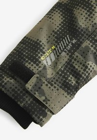 Tarnfarbener grüner Handschuh mit schwarzen Punktmustern, einem Klettverschluss und aufgedruckten Koordinaten in Gelb und Weiß am Bund.
