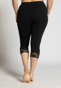 Černé capri legíny vyrobené z měkkého materiálu, s krajkovými detaily na lemu. Design je přiléhavý a končí těsně pod kolenem.