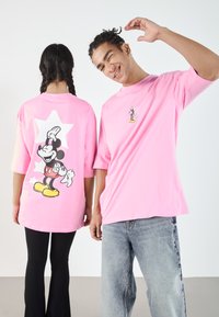 Rosa oversized t-skjorter har Mickey Mouse-grafikk både foran og bak. Den ene har en stjernemotiv bakgrunn, mens den andre har et lite brysttrykk.