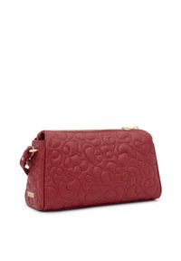 Czerwona skórzana torba na ramię z wytłoczonymi zaokrąglonymi wzorami, złotymi elementami metalowymi i zamknięciem na zamek. Posiada boczną metkę z napisem "TOUS." Kompaktowy design.