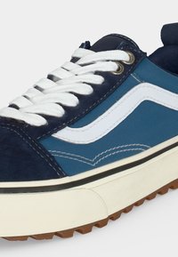 Niebieski i granatowy sneaker z białymi sznurówkami, białym paskiem bocznym, beżową podeszwą i widocznym brązowym bieżnikiem.