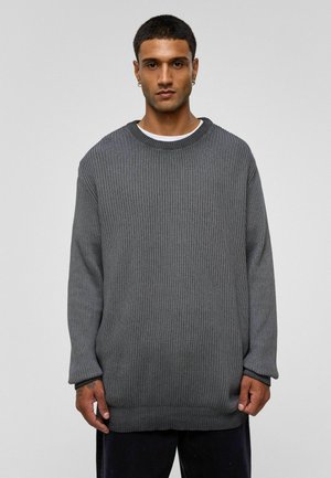 Grijze gebreide trui met lange mouwen, een ronde hals en een ribbeltextuur. Kenmerkt zich door een losse pasvorm en een stevige zoom, gedragen over een witte top.