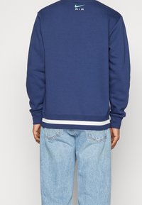 Marinblå sweatshirt med rund hals, långa ärmar och vita randiga detaljer vid fållen. Har "Nike AIR"-logotyp på övre ryggen.