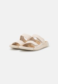 Sandali beige con due cinturini regolabili in velcro, una soletta sagomata e una suola leggera, progettati per comfort e facilità d'uso.