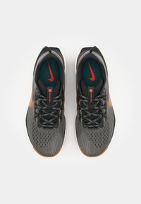 Czarno-szare buty sportowe z teksturowanym wierzchem, pomarańczowymi akcentami i zieloną wkładką. Posiadają wzorzysty design i czarne sznurowadła.