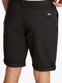 Calções pretos de algodão com um design de cintura média, bainhas enroladas e dois bolsos traseiros. Um pequeno logótipo é visível perto da cintura.
