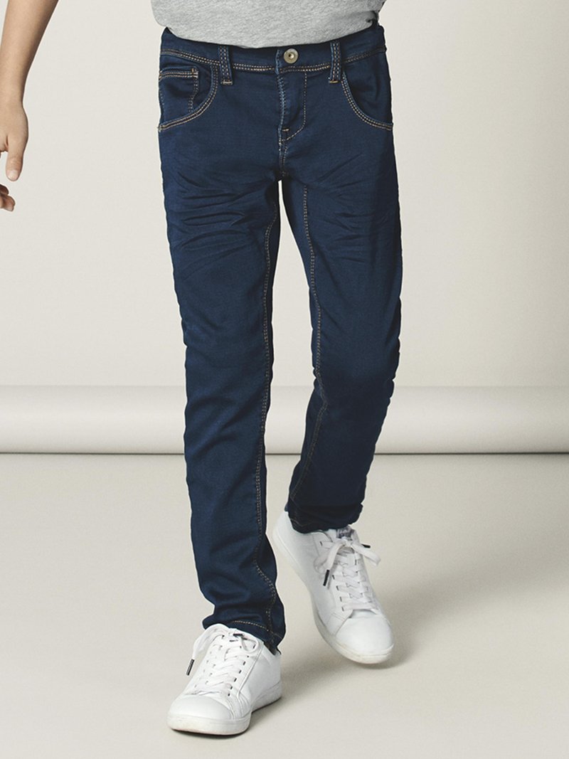 Mørkeblå denimjeans med slim fit, frontlommer med synlige sømmer og knappelukking. Kombinert med hvite joggesko.