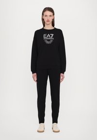 Fekete kapucnis pulóver és nadrág szett, elasztikus mandzsettákkal, fehér EA7 Emporio Armani logóval a mellkasán. Könnyű anyag, minimalista dizájn.