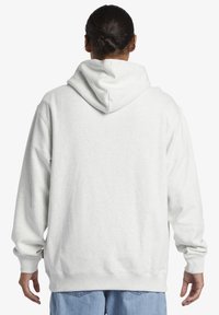 Lys grå hættetrøje med kengurulomme, ribbede manchetter og kant. Stoffet er blødt, med en glat tekstur og en afslappet pasform.
