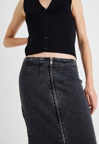 Svart ribbad ärmlös topp med v-ringning och sex knappstängningar, parat med en hög midja mörkgrå denimkjol med en frampaneldragkedja.