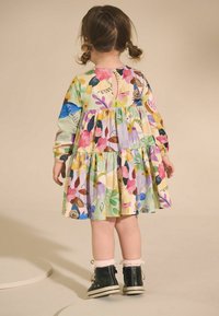 Robe à motifs floraux dans des couleurs pastel avec une jupe à plusieurs niveaux, fermeture à boutons au dos, complétée par des baskets montantes noires et des chaussettes blanches.