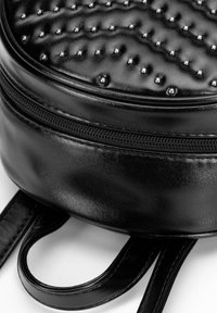 Mochila de cuero negro con forma redondeada, textura acolchada y acentos con tachuelas. Incluye un cierre de cremallera y dos correas planas en la base.