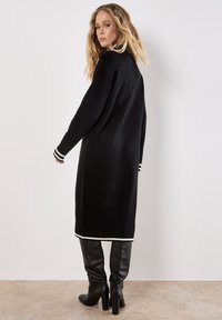 Schwarzes, übergroßes Strickkleid mit geripptem Saum und Bündchen, das weiße Streifenakzente aufweist und aus einem weichen Strickmaterial besteht.