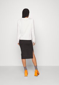 Maglietta bianca a maniche lunghe con spalle voluminose, abbinata a una gonna midi a coste grigia scura con uno spacco laterale. Tacchi chunky arancioni brillanti.