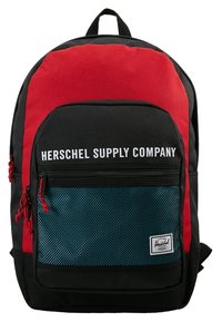 Sac à dos noir et rouge avec une poche avant en filet, arborant le logo blanc "Herschel Supply Company", compartiments zippés et tissu résistant.