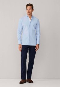 Chemise bleu clair à boutons avec manches longues, associée à un pantalon bleu marine foncé et des chaussures marron. Design simple, coupe droite, sans motifs visibles.