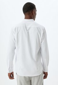 Camisa blanca de manga larga con un cuello clásico, detalle de yugo en la parte posterior y puños abotonados. Fabricada en una tela suave y ligera.