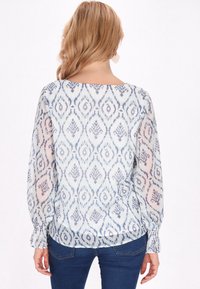Blusa leggera azzurro chiaro con un motivo a diamante ripetuto, maniche lunghe e scollo a barco. Tessuto morbido e trasparente con polsini arricciati.