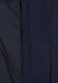 Lekka kurtka w kolorze granatowym z widocznym przeszyciem. Posiada ukrytą kieszeń i gładką fakturę. Brak widocznych wzorów czy ozdób.