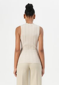 Beige ribbattu sleeveless toppi, jossa on korkeakauluksinen muotoilu, ominaisuutena tiukka istuvuus ja teksturoitu materiaali, yhdistettynä leveälahkeisiin beigen värisiin housuihin.