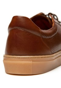 Brązowy skórzany but z teksturowaną powierzchnią, perforowanym wzorem i gumową podeszwą. Obcas ma gładkie wykończenie i jest lekko zaokrąglony.