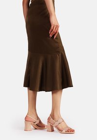 Sandali con tacco in suede rosa, dotati di tacco a blocco, punta aperta e decorazioni floreali. Indossati con una gonna midi marrone con orlo svasato.