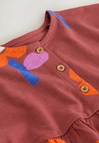 Bomulds kjole i rustfarve med flerfarvede geometriske mønstre. Har træknapper og en rynket bund for et tekstureret udseende.