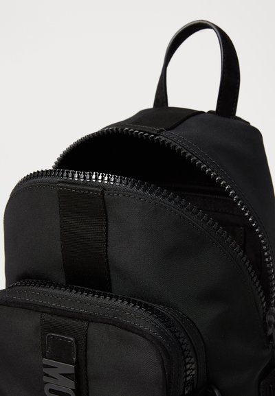 Rucsac negru din nylon, cu compartimente cu fermoar dublu, accente din webbing și o mânere pe partea de sus. Textură netedă cu un design minimalistic.