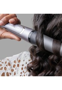 Sølv krølljern med elegant design, sylinderformet fat og svarte detaljer. Håret er viklet rundt fatet, noe som viser frem definerte krøller.