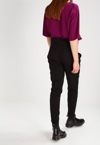 Top corto morado de mangas cortas con un corte holgado, combinado con pantalones negros ajustados y botas de tobillo brillantes negras con acentos amarillos.