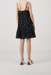 Mustat hihattomat mekko, jossa on kerroksellinen helma ja kultaiset timanttikuvioinnit. Yhdistettynä rentoihin lenkkareihin ja teksturoituihin nilkkasukkiin.