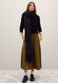 Sciarpa di lana nera avvolta intorno al collo; abbinata a una maglia nera a maniche lunghe e a una gonna color senape lunga fino al ginocchio; scarpe nere con suole spesse.