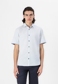 Camisa de botão com mangas curtas em azul claro, com uma textura suave, apresentando um padrão tecido e botões escuros. Estilizada com uma bainha curvada.