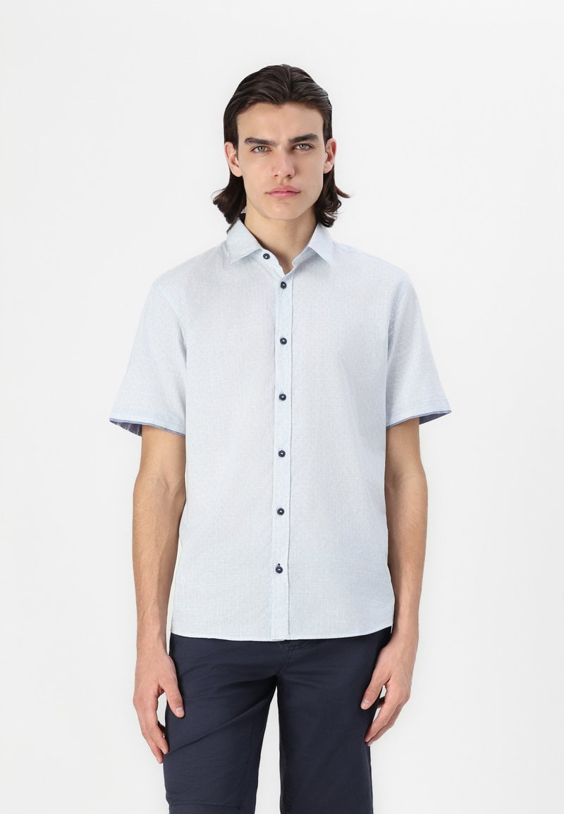 Camisa de botão com mangas curtas em azul claro, com uma textura suave, apresentando um padrão tecido e botões escuros. Estilizada com uma bainha curvada.