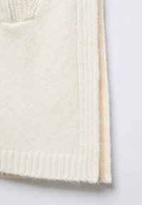 Gefalteter, cremefarbener Wollpullover mit gerippten Bündchen und weichem, strukturiertem Strickstoff auf hellem Hintergrund.