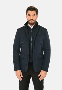 Giacca a vento blu navy con design strutturato, chiusura con zip e diverse tasche; texture trapuntata con colletto interno in contrasto.