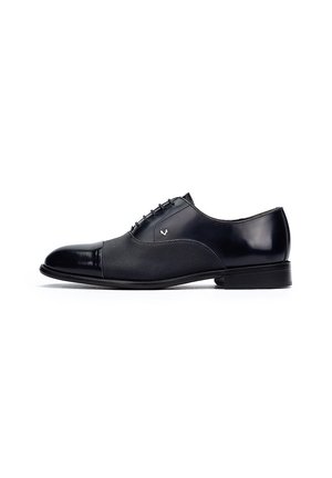Zapato de vestir negro con puntera de cuero liso, panel de malla texturizada y suela de perfil bajo con diseño de cordones.