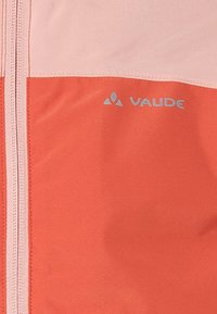 Chaqueta de concha blanda con bloques de color en coral y rosa claro, con un prominente logo plateado. Cierre delantero con cremallera y textura suave, ligeramente brillante.