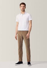 Polo shirt bianco a maniche corte abbinato a pantaloni beige chiaro e sneakers nere. Il polo presenta un colletto classico e un design pulito.