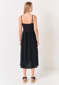 Abito midi nero con spalline sottili, corpetto aderente e gonna svasata. Realizzato in tessuto leggero, presenta un design semplice e un'apertura sulla schiena.