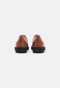 Brown leather shoes with a rounded shape, featuring a contrasting black rubber sole and minimal stitching details on the back.