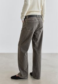Gray wide-leg jeans with a high waist, featuring back pockets and a clean stitch detail, paired with black flat shoes.