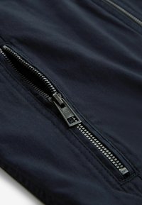 Metal zipper partially open on dark navy fabric, showing detailed teeth and stitching.