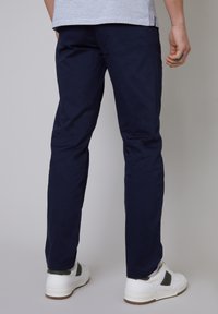 Pantalons en coton bleu marine avec une coupe droite, texture lisse et détails de couture minimaux, associés à des baskets blanches.